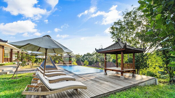 A wooden deck with lounge chairs and umbrellas, a pool, and a gazebo. - Kana Village Villa by Kozystay (Tabanan)
