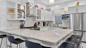 Een moderne keuken met een centraal kookeiland, een paar barkrukken, roestvrijstalen apparatuur en hanglampen.
