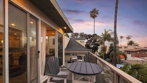 Een balkon met een tafel en stoelen, een schuifpui en uitzicht op palmbomen en huizen.