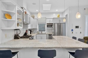 A modern kitchen with white cabinetry, a central island, stainless steel appliances, pendant lighting, and a dining area with chairs.