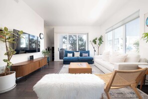 Ein modernes Wohnzimmer mit Sofa, Couchtisch und einem weißen, flauschigen Hocker.