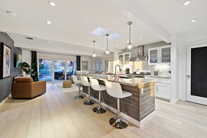 Cozinha moderna com ilha central, banquetas, iluminação pendente e vista para o exterior.