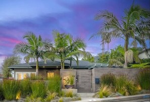 Uma casa moderna com cerca de madeira, palmeiras e um jardim bem cuidado.