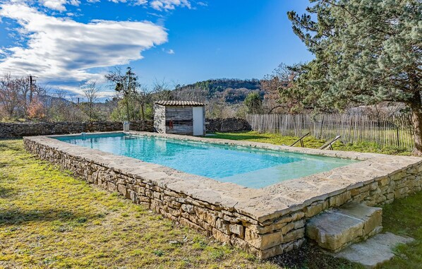 pool surrounded by lush greenery and a rustic stone building in the background.