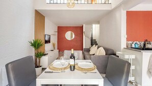 Ein zeitgemäßer Essbereich mit einem weißen Tisch für zwei Personen, einer Champagnerflasche und einem an der Wand befestigten Fernseher.