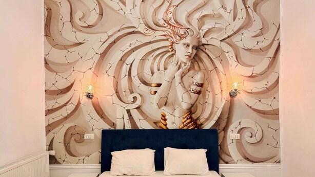 Un dormitorio con una cama grande, cabecera, mesitas de noche y un mural en la pared.