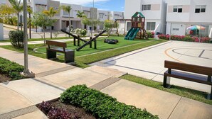 A playground with a slide and swings, surrounded by a well-maintained lawn and pathways. - Casa con alberca propia-Almarena (Mazatlán)