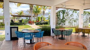 An outdoor patio with wooden tables and chairs, surrounded by lush greenery and palm trees. - Casa con alberca propia-Almarena (Mazatlán)