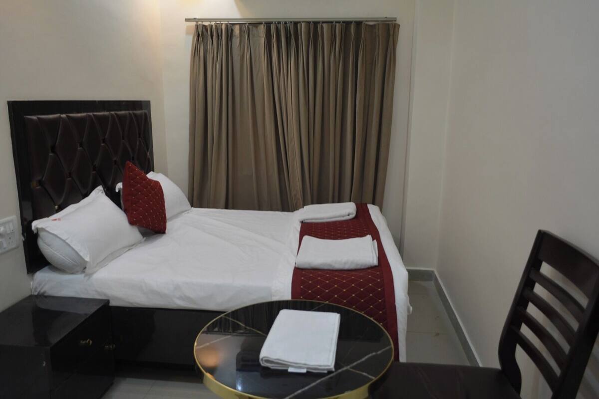 Ein Hotelzimmer mit einem Bett, einem kleinen runden Tisch mit Tablett, einem Sessel und einem Fenster mit Vorhängen.