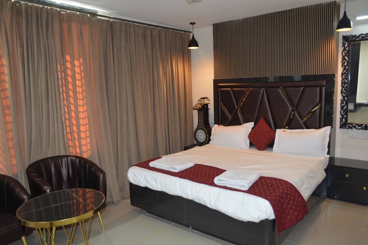 Ein Hotelzimmer mit einem großen Bett, einem runden Tisch, einem Stuhl, einer Uhr und einem Spiegel an der Wand.