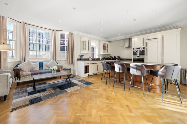 A modern kitchen with white cabinetry, a central island, and bar stools. - Knightsbridge Luxury: 3BR/3BA, AC, Patio (London)