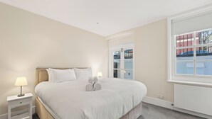 Une chambre à coucher avec un grand lit, des tables de chevet et une fenêtre donnant sur des immeubles.