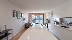 A modern kitchen with a large island, a dining area with a sofa, and a view through a sliding glass door to the outdoors.