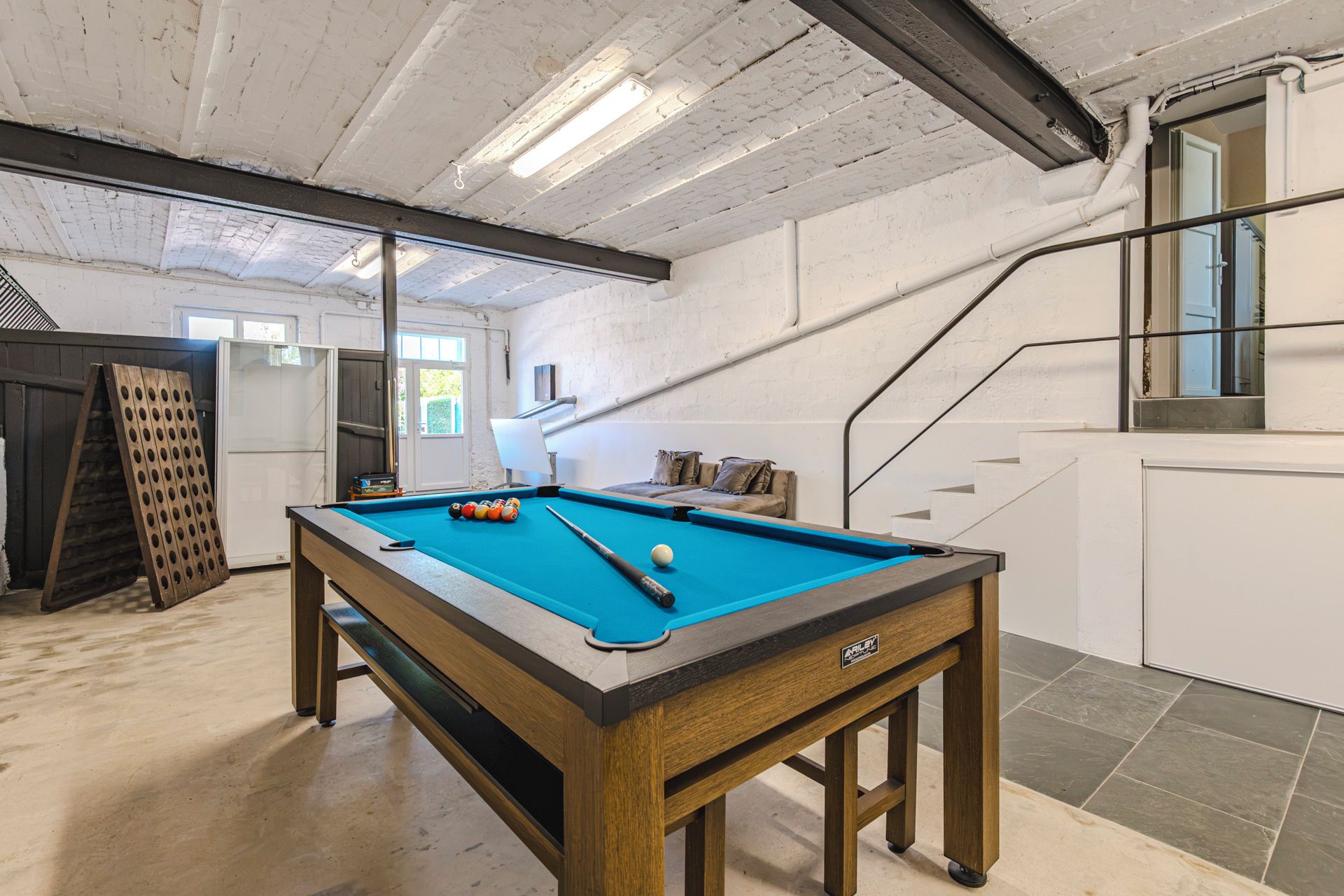 Une table de billard avec des billes, un banc en bois et un escalier.