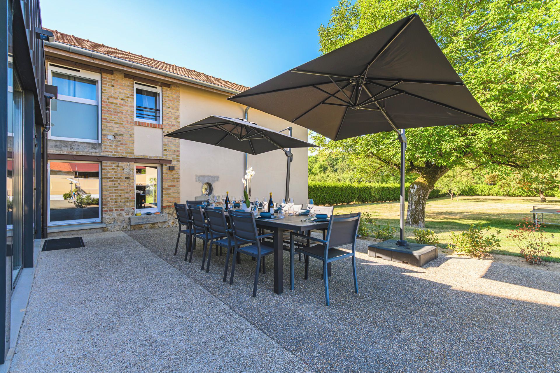 An outdoor patio with a table set for dining, surrounded by chairs and large umbrellas.