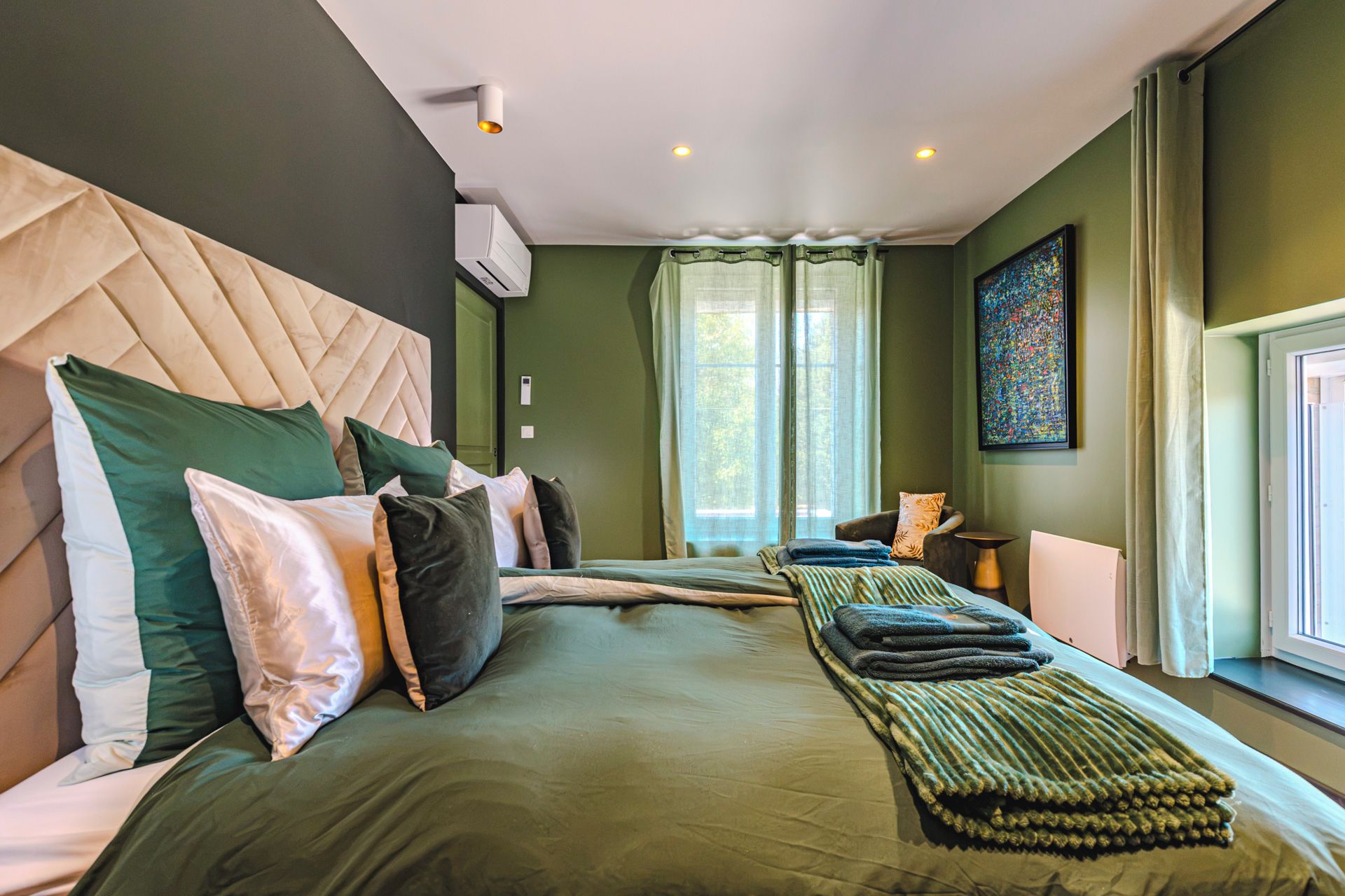 Een hotelkamer met een groot bed, een hoofdeinde, een raam met gordijnen en een schilderij aan de muur.