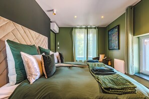 A hotel room with a large bed, a headboard, a window with curtains, and a painting on the wall.