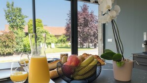 Une table de petit-déjeuner avec un verre de jus d’orange, un panier de fruits et une plante en pot.