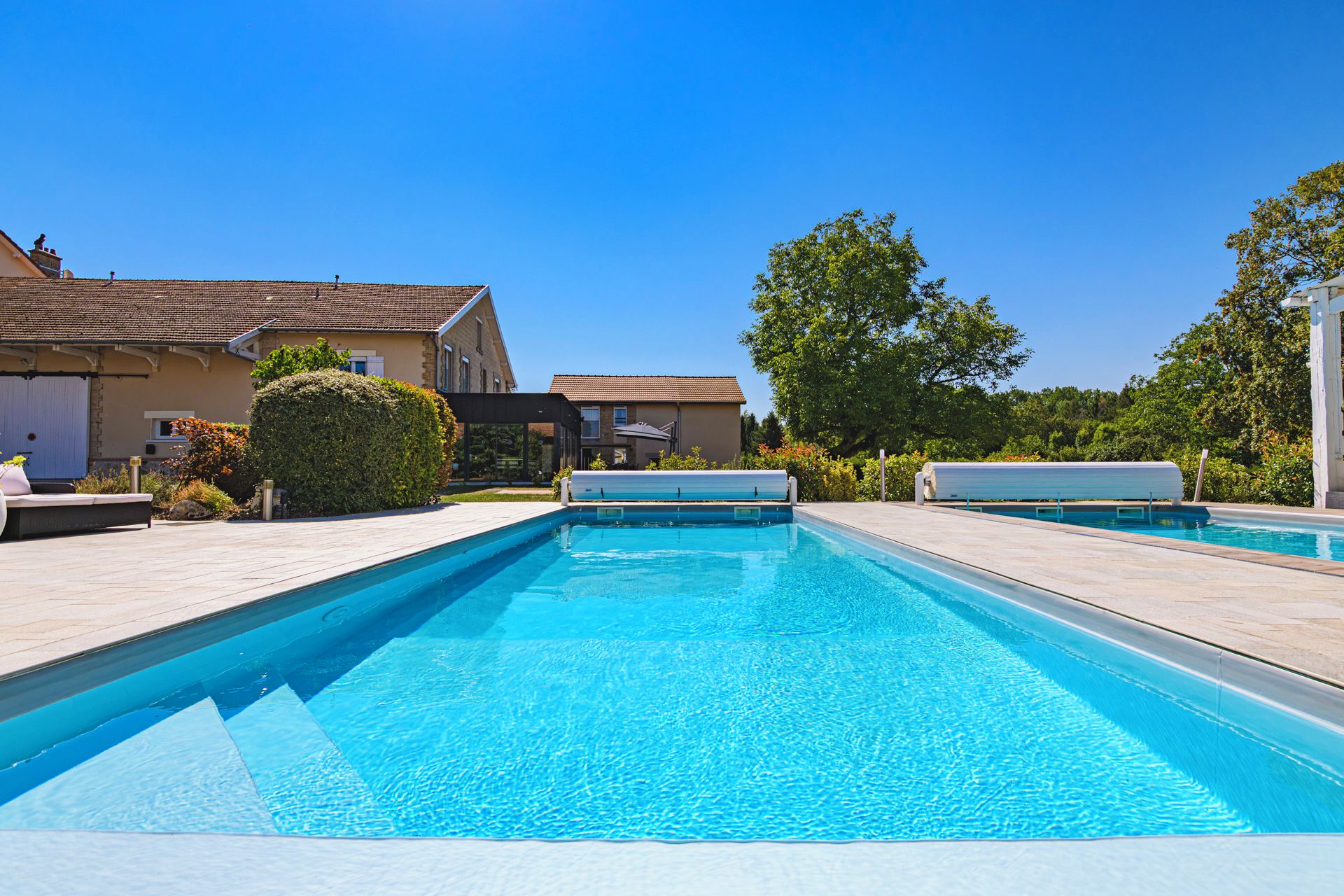 A swimming pool with a clear blue water surface, surrounded by a paved deck.