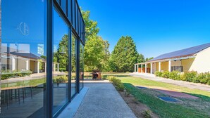 Un bâtiment moderne doté de grandes fenêtres en verre, d’un espace extérieur couvert aménagé en coin salon et d’une pelouse bien entretenue.