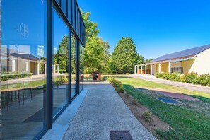 A modern building with large glass windows, a covered outdoor seating area, and a well-maintained lawn. - L'Artbanne - The Hestia house (Saint-Hilaire-le-Petit)