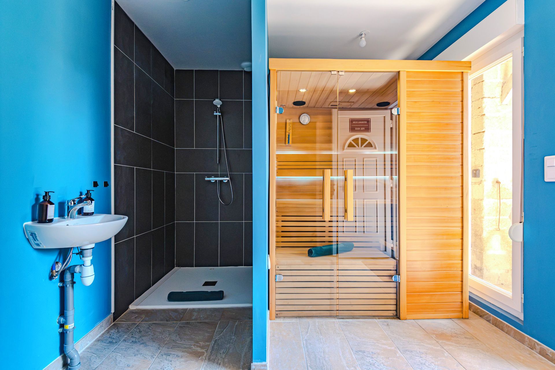 Een moderne badkamer met een douche, een wastafel en een houten deur naar de douchecabine.