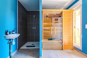 Un baño moderno con ducha, lavamanos y una puerta de madera que da a la zona de la ducha.