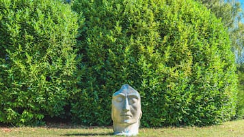 Una escultura de piedra en un área con césped y un seto verde denso al fondo.