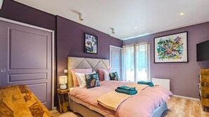 Une chambre à coucher comprenant un lit, des tables de chevet, une commode, une petite table en bois et une fenêtre avec des rideaux.