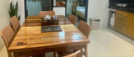 Un comedor con una mesa de madera, seis sillas y una zona de cocina con armarios y un televisor.