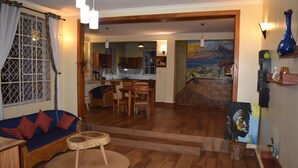 A living room with a sofa, dining table, chairs, and a kitchen in the background. - kili Kivuli  (Moshi)