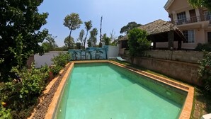 A rectangular swimming pool with a tiled edge, surrounded by a garden with various plants and a wall with a mural. - kili Kivuli  (Moshi)