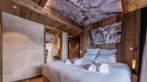 Un dormitori modern amb un llit gran, sostre de fusta i un quadre d'un paisatge nevós.