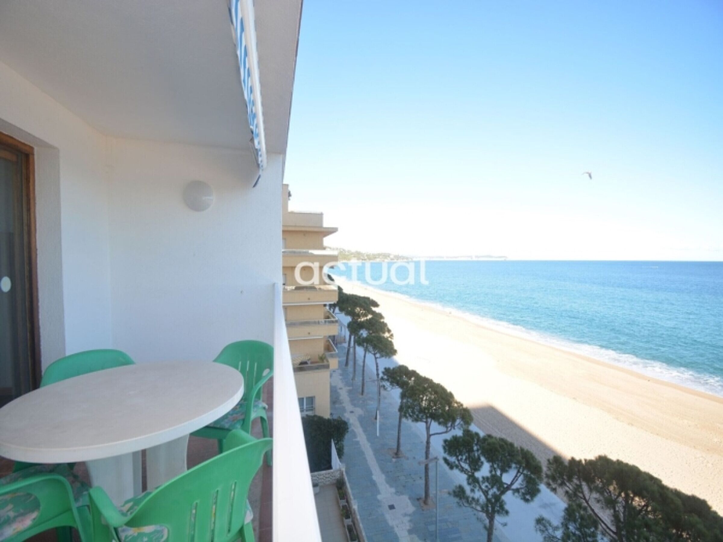 A balcony with a table and chairs, overlooking a beach with a clear sky.