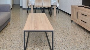 A living room with a grey sofa, a wooden coffee table, a TV on a wooden cabinet, and a dining area with chairs and a table. - Cozy apartment with WiFi and parking in Platja d'Aro (Platja d'Aro)