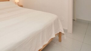 A bed with a white bedspread, wooden headboard, and a nightstand with a lamp.