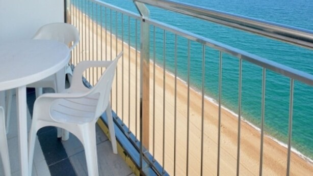 A balcony with a white table and chairs, overlooking a beach and the sea.