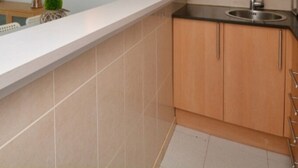 A modern kitchen with a white countertop, beige tiles, and wooden cabinets.