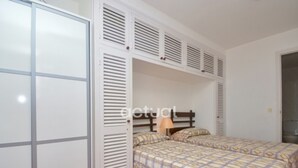 A bedroom with two beds, a wardrobe, and a door with louvered panels. - 1-Bed Apt in Platja d'Aro with Terrace & Parking (Platja d'Aro)