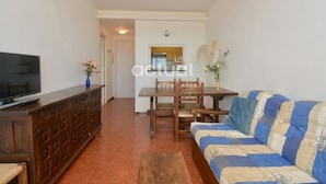 A living room with a sofa, a wooden cabinet, a television, and a dining table with chairs. - 1-Bed Apt in Platja d'Aro with Terrace & Parking (Platja d'Aro)