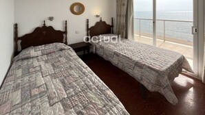 Una habitación con dos camas, un ventanal con vista al mar y un espejo redondo pequeño en la pared.