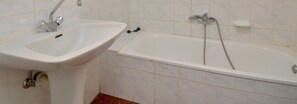 A bathroom with a white sink and bathtub, tiled walls, and a visible pipe under the sink.