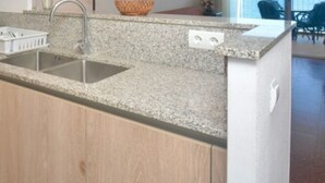 A kitchen with granite countertops, a stainless steel sink, wooden cabinets, and a coffee maker. - 1-Bedroom Apartment with Terrace & Parking in Platja d'Aro (Platja d'Aro)