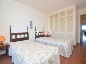 A bedroom with two beds, a nightstand, a lamp, and a wardrobe.
