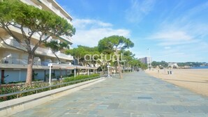 Uma passarela pavimentada com uma praia ao fundo, árvores e um edifício com varandas.