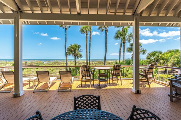 A covered outdoor area with a wooden deck, lounge chairs, and a table.