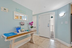A hallway with a reception desk, a digital clock, a mirror, a door, and a wall-mounted light fixture.