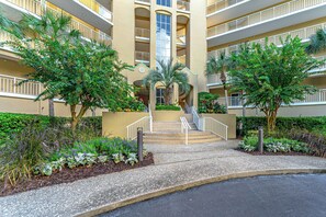 A multi-story hotel with a central courtyard, balconies, and a variety of greenery.