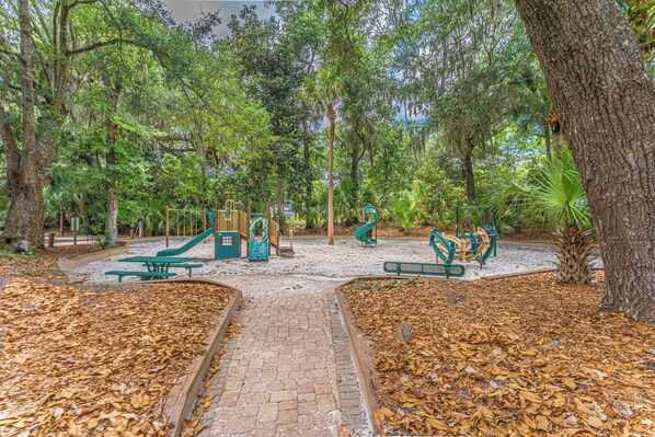 Un parque infantil con toboganes y columpios rodeado de árboles y cubierto de hojas secas.