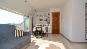 Ein Wohnzimmer mit einer Couch, einem Esstisch mit Stühlen, einer Holztür und einem Bücherregal.